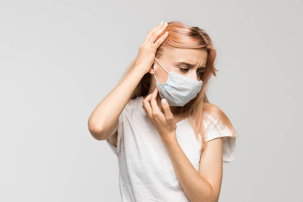 Isolated studio portrait of young beautiful woman with medical mask in white t-shirt scratching neck/irritation, sensitive skin, allergy symptoms, rhinitis, cold, itch, healthcare and medicine concept - Photo, Image