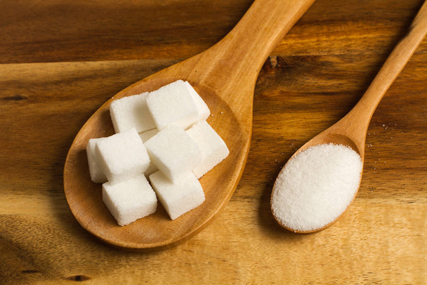 Zuckerwürfel auf einem Holzlöffel und weißer Zucker auf einem Holzlöffel - Foto, Bild