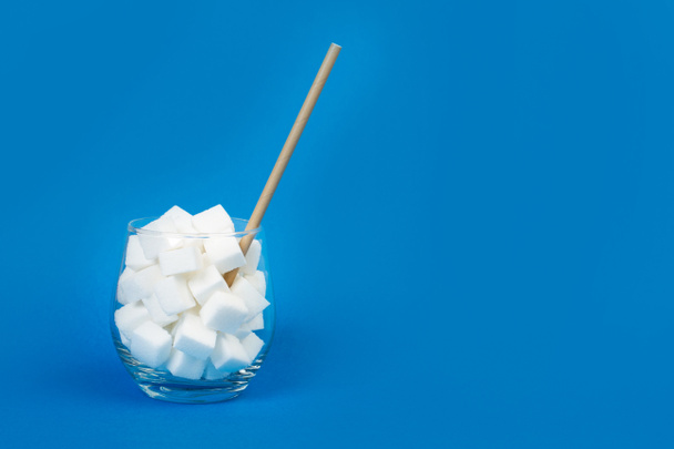 White sugar cubes in a glass with a straw and on a blue background - Foto, imagen