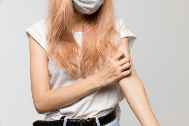 Ізольований студійний портрет молодої красивої жінки з медичною маскою в білій футболці подряпає свербіж рукою, подразнення, чутливу шкіру, симптоми алергії, риніт, холод, охорона здоров'я та концепція медицини
. - Фото, зображення