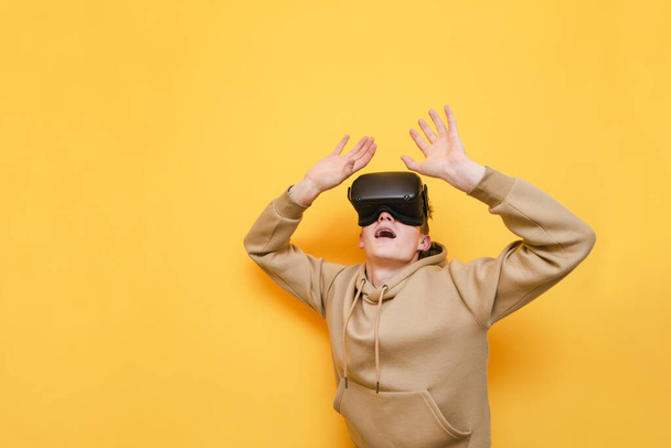 Portrait of shocked young man in VR glasses isolated on yellow background, looking up with surprised face. Copy space - Fotoğraf, Görsel
