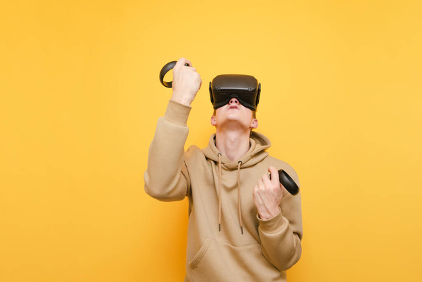 Joyful gamer em um capacete VR e com controladores em suas mãos tem o prazer de ganhar o jogo de vídeo. Jovem a jogar RV no capacete, isolado. Conceito de realidade virtual
. - Foto, Imagem