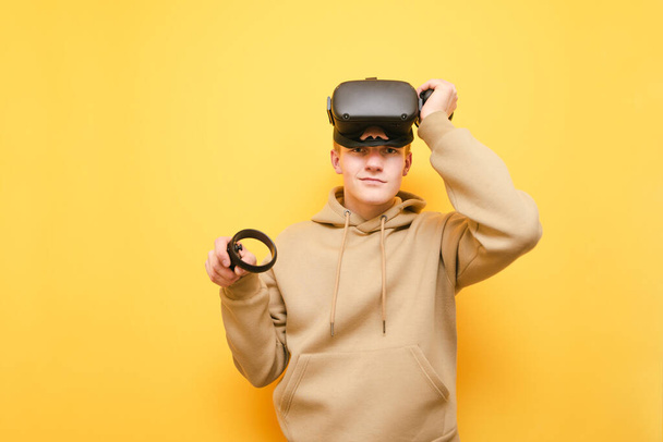 Portrait of positive guy in VR helmet on head isolated on yellow background, posing at camera. Cheerful young male gamer playing VR games, smiling and looking at the camera - Fotoğraf, Görsel