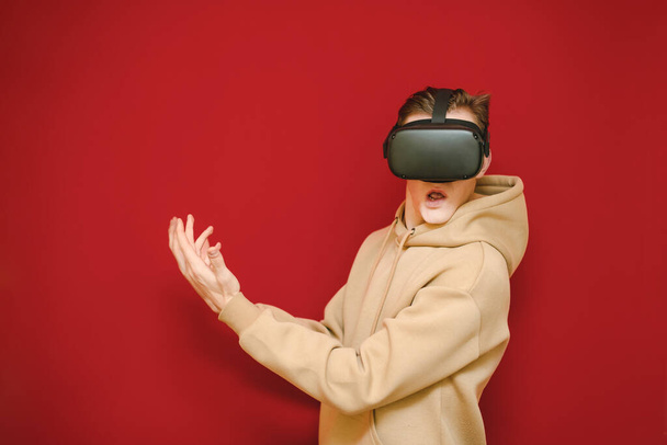 Homme drôle avec casque VR sur la tête isolé sur rouge regarde dans la caméra avec le visage choqué. Jeune homme essayant la technologie VR pour la première fois, il est très surpris. Concept de réalité virtuelle
 - Photo, image