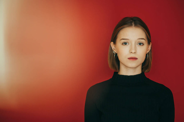 Creative portrait of a pretty girl in casual clothes, wearing a black sweater, standing on a red background and looking intently at the camera. Cute model isolated on bright background. - Fotoğraf, Görsel