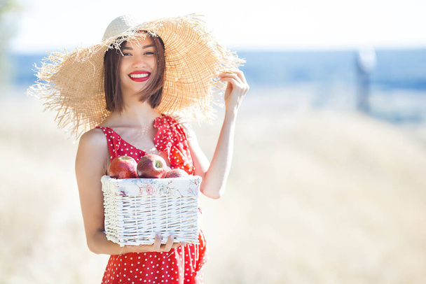 Portrait of young beautiful woman wearing straw hat on summer background. Female with fresh apples on the nature. - Φωτογραφία, εικόνα