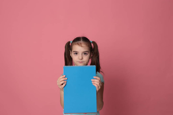 menina engraçada de oito anos de idade e uma folha de papel colorido espaço livre para escrever em um fundo rosa pálido
 - Foto, Imagem