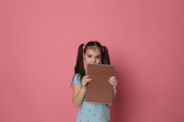 funny girl of eight years old and a colored sheet of paper free space for writing on a pale pink background - Fotoğraf, Görsel