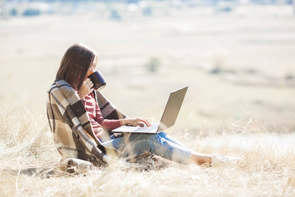 Junge attraktive Frau, die draußen am Laptop arbeitet. Frau mit natürlichem Hintergrund, die ihren freien Job am PC ausübt. Fernbedienung im Urlaub. - Foto, Bild