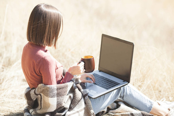 Jovem mulher atraente trabalhando no laptop ao ar livre. Mulher em fundo natural fazendo seu trabalho freelance no PC. Vorker remoto em férias
. - Foto, Imagem
