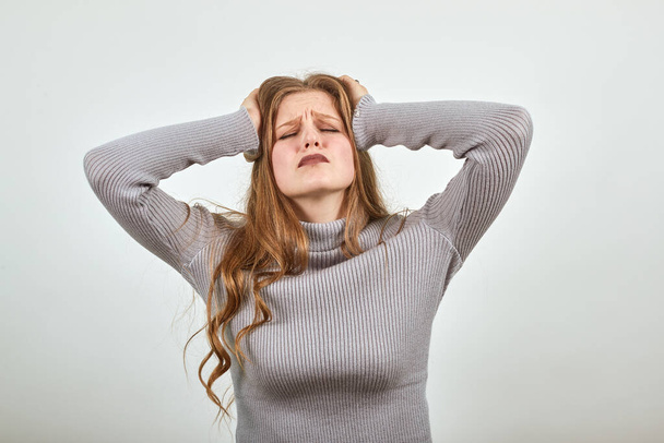 rothaarige Frau im grauen Pullover schneidet Kopf mit den Händen, was Kopfschmerzen verursacht - Foto, Bild