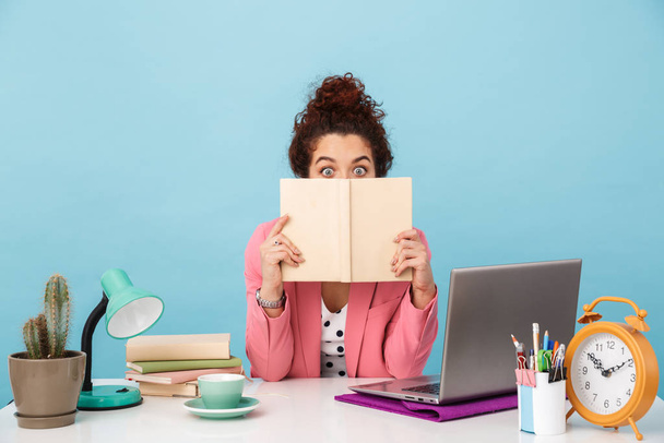 Image of surprised woman holding book and looking at camera while working - Foto, Bild