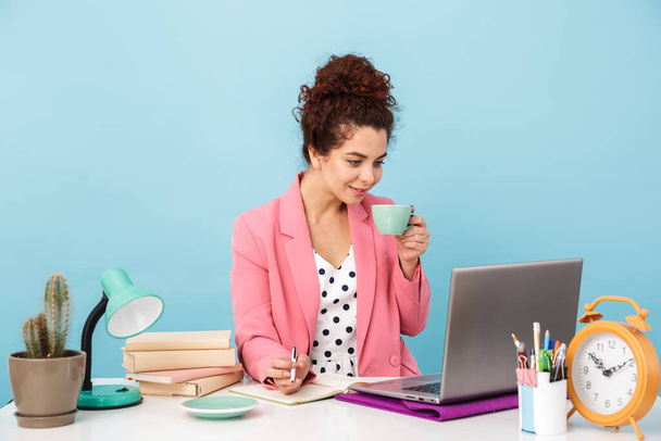 Kuva houkutteleva nainen käyttää kannettavaa tietokonetta ja juo kahvia työskennellessään
 - Valokuva, kuva