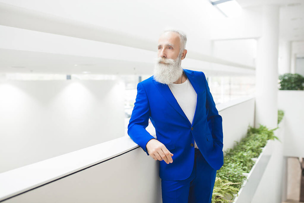 Красивый стильный мужчина в бизнес-центре. Бизнесмен, стоящий на нейтральном офисном фоне, зрелый уверенный в себе человек в синем костюме
. - Фото, изображение