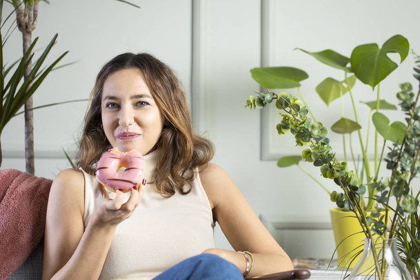 Young woman eating pink chocolate chips donut - Foto, afbeelding