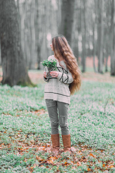 beautiful young girl woman walking through the green forest in spring, holding glass ar with white spring flowers - Valokuva, kuva