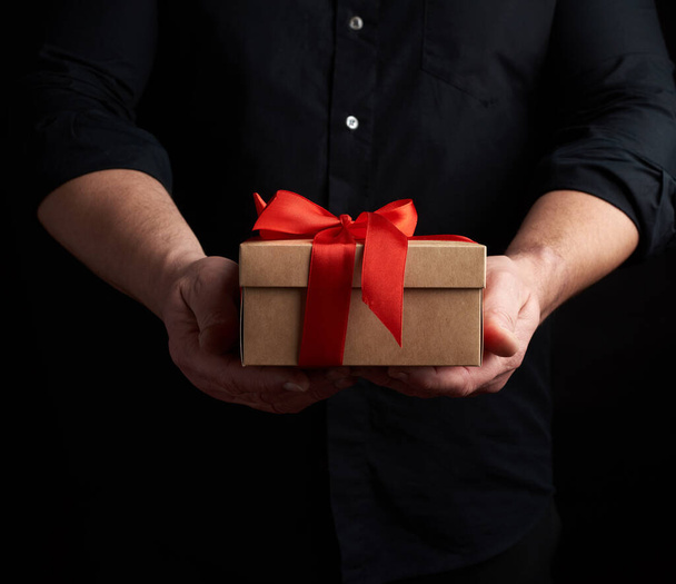 adult man in a black shirt holds in his hand a square brown boxl - Foto, Imagem
