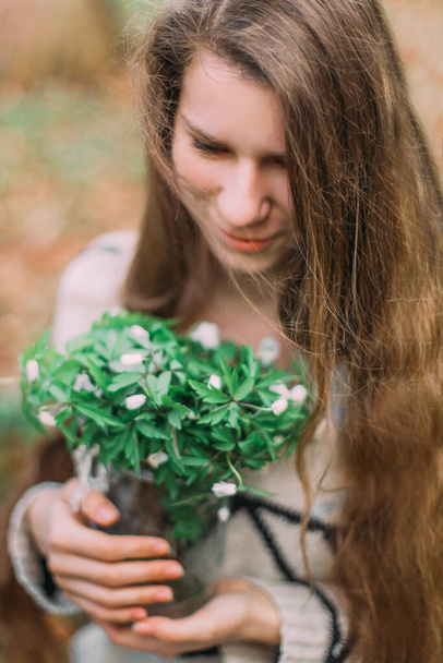 pretty girl holding white spring flowers walking through the green forest - Fotografie, Obrázek