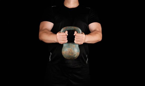 взрослый сильный спортсмен в черной одежде, держащий железный гирь
 - Фото, изображение