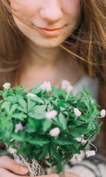 pretty girl holding white spring flowers walking through the green forest - Foto, imagen