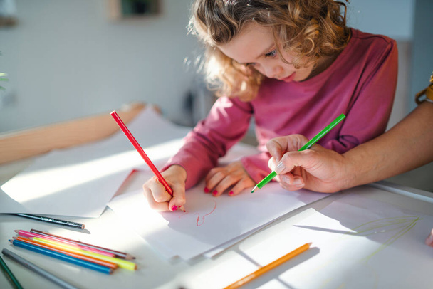 A cute small girl with mother indoors at home, drawing pictures. - Foto, afbeelding