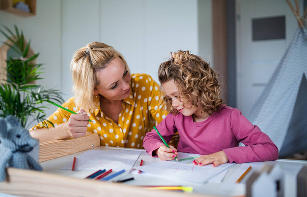 A cute small girl with mother indoors at home, drawing pictures. - Foto, Bild