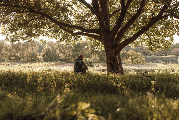 Caminante irreconocible descansando bajo el árbol en la naturaleza
 - Foto, imagen
