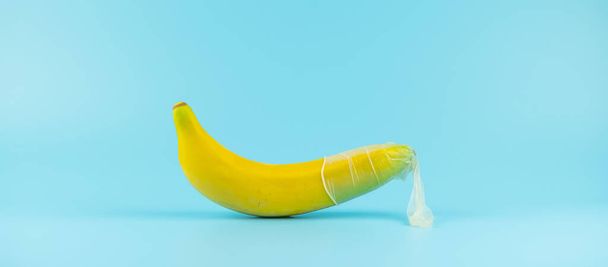 Μεταχειρισμένα Condom και μπανάνα σε μπλε φόντο. Ασφαλές σεξ και απάτη αγάπης - Φωτογραφία, εικόνα