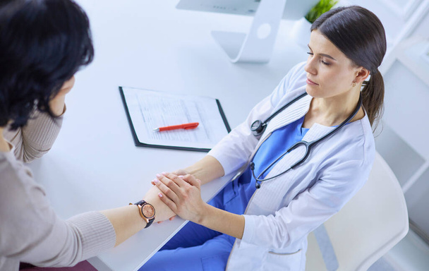Female doctor calming down a patient at a hospital consulting room, holding her hand - Foto, Imagem