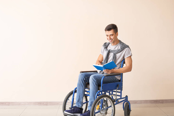 Αναπηρικός νεαρός άνδρας σε αναπηρικό καροτσάκι ανάγνωση βιβλίο κοντά στον τοίχο χρώμα - Φωτογραφία, εικόνα