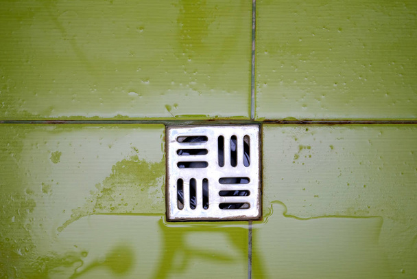 Duschrost auf dem Boden. Draufsicht Abflussloch im Badezimmer. Nasse grüne Fliesen und Metallbodengitter. - Foto, Bild