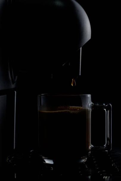 The coffee machine makes latte in a glass cup on a dark background. Cappuccino, cooking, cup, glass, morning, breakfast, steam, hot drink, brewing, - Fotoğraf, Görsel