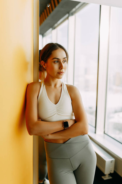 Stands after a workout with a watch. Portrait of a sports girl in the gym. Beautiful white girl for advertising.  - 写真・画像