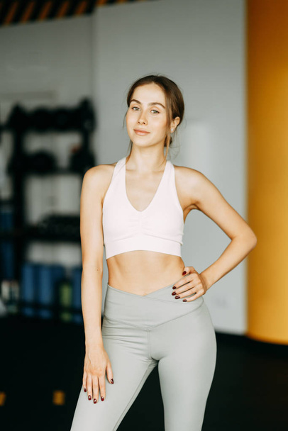 Stands after a workout with a watch. Portrait of a sports girl in the gym. Beautiful white girl for advertising.  - Foto, Imagen