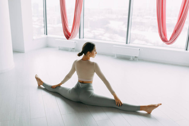 Stretching exercises on the floor and in the air. Beautiful girl athlete sitting on the twine. Room for a yoga workout with hammocks.  - Fotografie, Obrázek