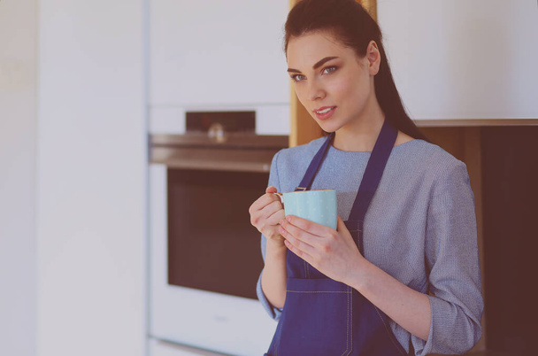Portrait of young woman with cup against kitchen interior background - Φωτογραφία, εικόνα