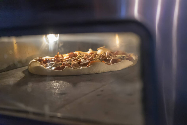 El cocinero pone pizza cruda en una pala en el horno de la cocina. Cocinar una comida rápida en una pizzería
. - Foto, Imagen
