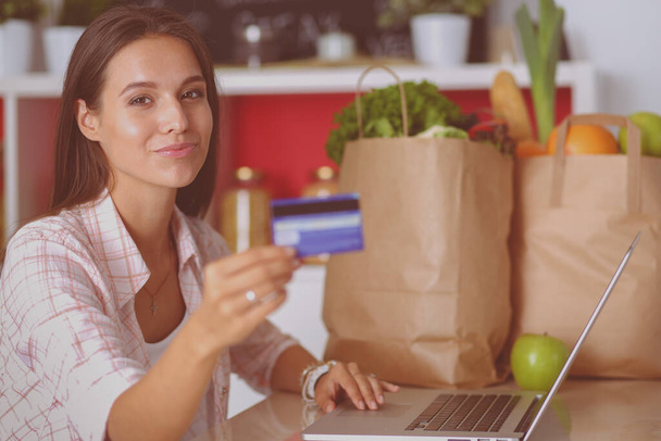 Mujer sonriente compras en línea utilizando tableta y tarjeta de crédito en la cocina. Mujer sonriente
 - Foto, Imagen