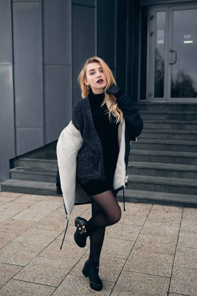 Girl in a black dress in the winter on a background of a dark building - Foto, Imagem