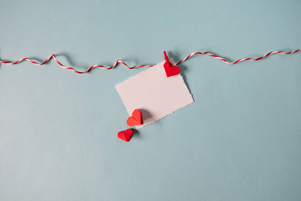 Rote Origami-Herzen auf Seil mit Wäscheklammern auf pastellblauem Hintergrund. Platz für Text, Kopierraum. Minimales Valentinstag-Konzept. - Foto, Bild