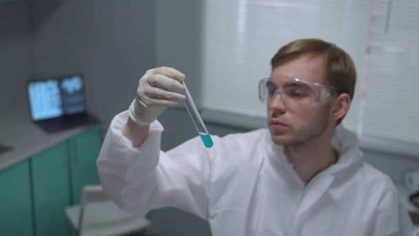 Cámara lenta, químico en tubo protector de la sacudida de la ropa de trabajo con líquido azul en el laboratorio
 - Foto, Imagen