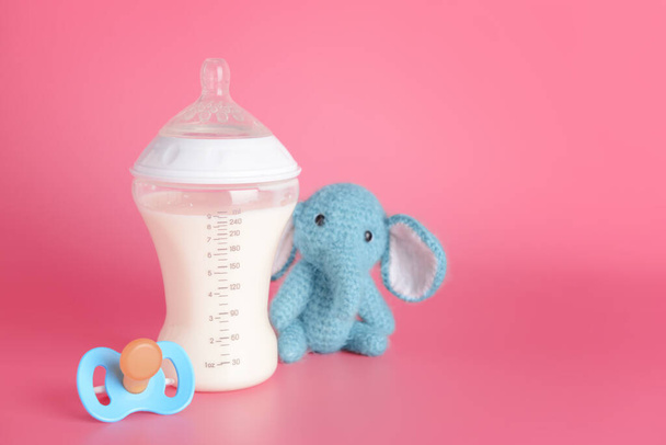 Botella de leche para bebé y juguete con chupete sobre fondo de color
 - Foto, Imagen