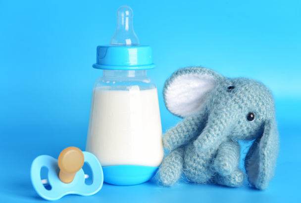 Botella de leche para bebé y juguete con chupete sobre fondo de color
 - Foto, Imagen