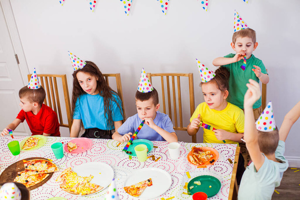 Dzieci świętują urodziny pizzą w kawiarni. Urodzinowe. Cute dzieci w kapeluszach urodzinowych zabawy razem - Zdjęcie, obraz