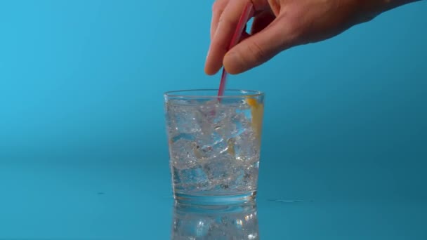Крупним планом рука змішування води в склянці на синьому фоні Природньо газована мінеральна вода з лимоном і льодом в склянці
 - Кадри, відео