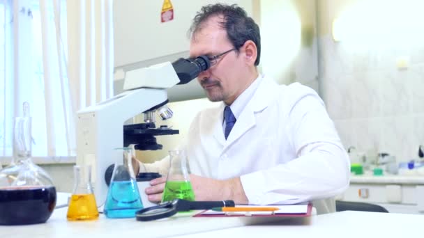 Kemisti hullu. Hullu tiedemies tekee kokeita tieteellisessä laboratoriossa. Suorittaa tutkimusta mikroskoopilla
. - Materiaali, video