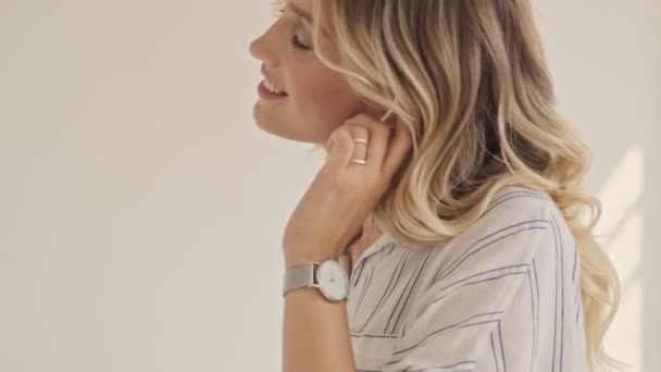 A nice smiling woman with blond hair is enjoying listening to the music with wired headphones in white office - Filmagem, Vídeo