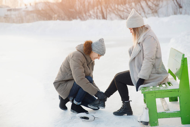 男は冬に雪の背景に美しい若い女の子へのリンクのための白いフィギュアスケートを置くのに役立ちます,コンセプトはケア愛です,人々の関係 - 写真・画像