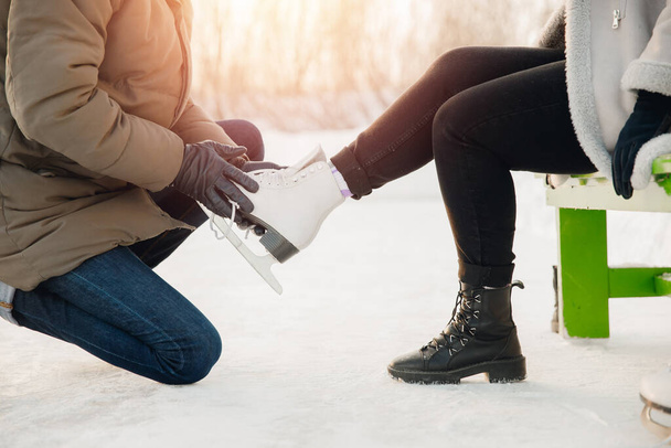 Man helps to put on white figure skates for rink to beautiful young girl on background of snow in winter, concept is care love, relationship between people - Photo, Image