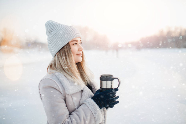 Beautiful happy woman outdoor winter. Laughing girl with hot drink tea or coffee with snowfall - Photo, Image
